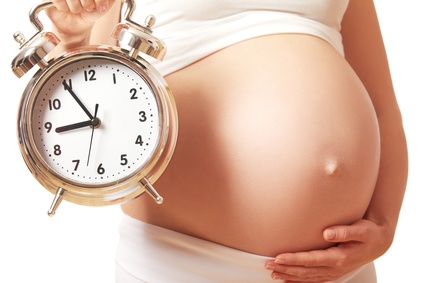 the concept of pregnancy. belly tummy of a pregnant woman and alarm clock on a white background