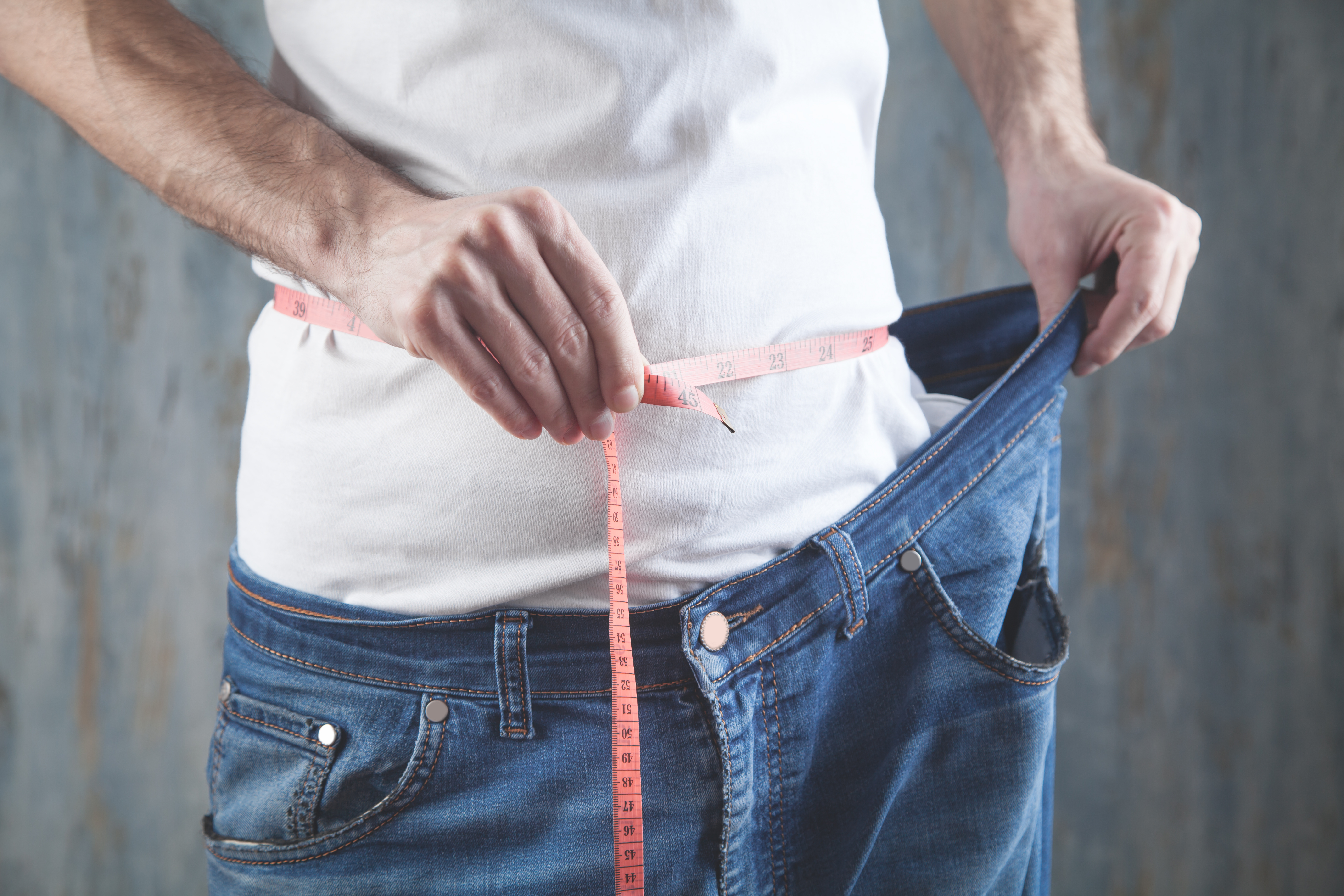 Man measure his belly and showing big jeans. Losing weight